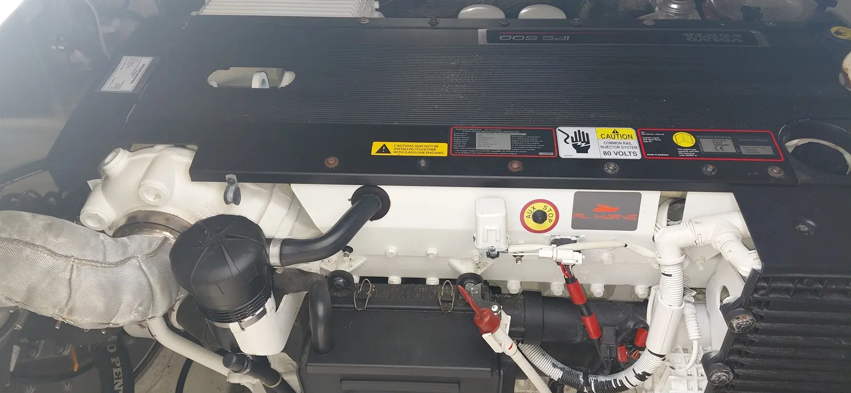Marine engine components with auxiliary stop button, warning labels, and various hoses visible on a boat engine compartment.