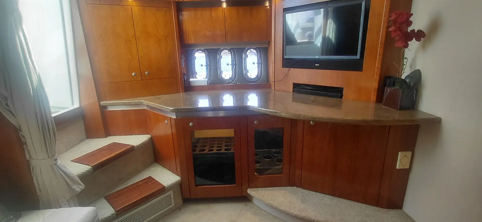 Modern wooden cabinetry with a granite countertop, TV, and staircase leading to a boat's interior space.