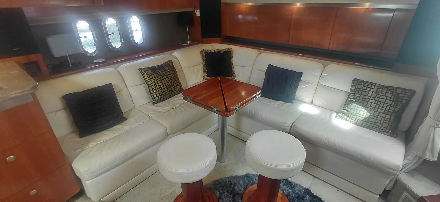 Modern yacht interior featuring a white leather sectional sofa with decorative pillows, a wooden table, and a cozy atmosphere.