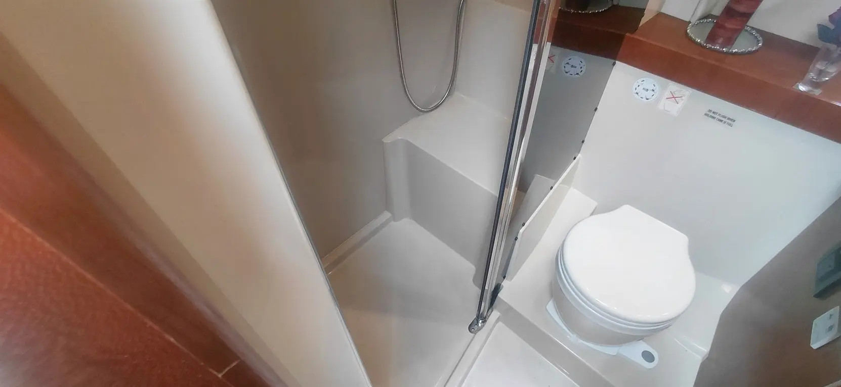 Compact bathroom featuring a shower area, toilet, and decorative shelf with a flower vase. Clean and modern design.
