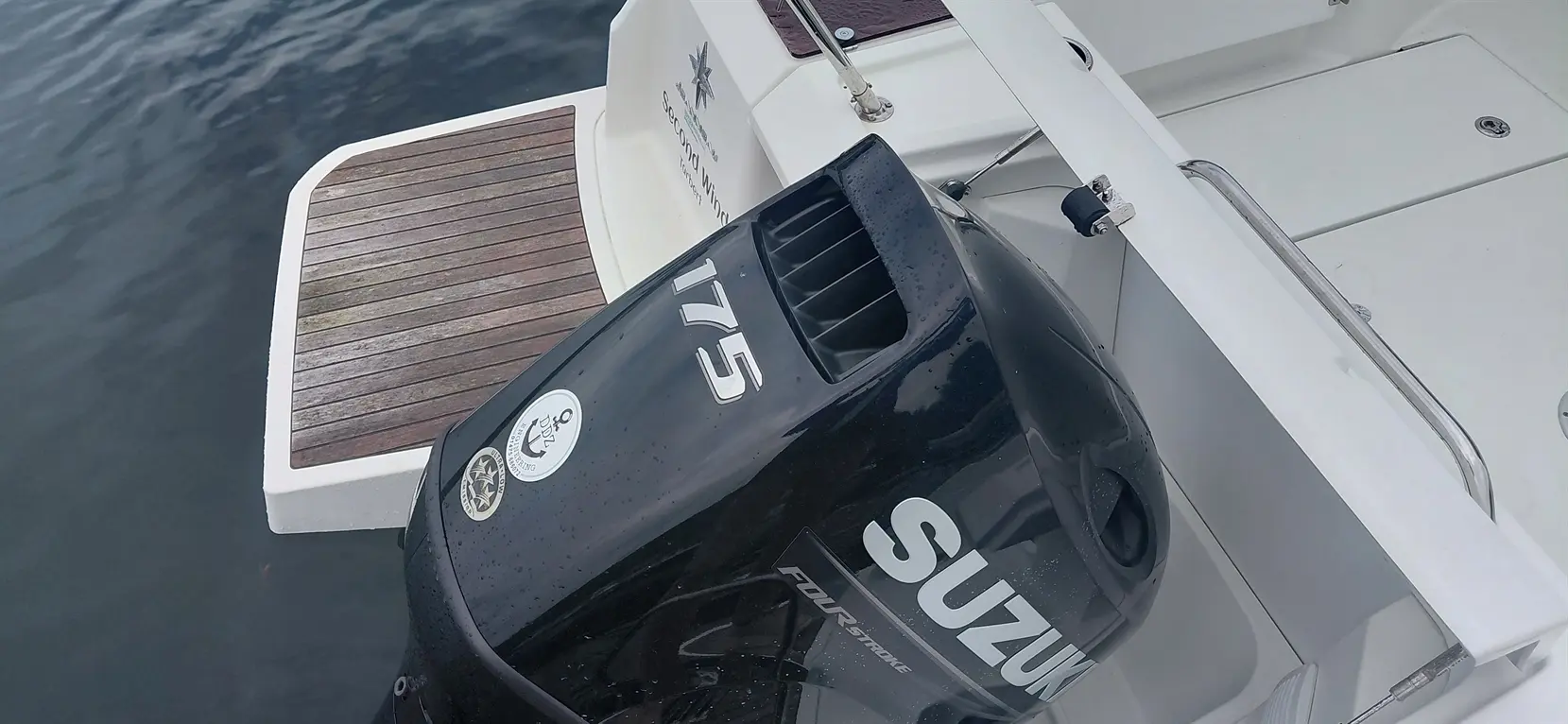 Suzuki 175 four-stroke outboard motor on a boat, with wooden platform and water surface in the background.