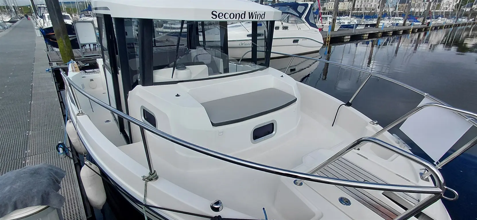 A white boat named "Second Wind" is docked, showing the rear deck and marina with boats in the background.