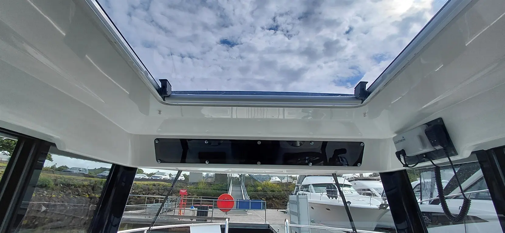 View of a boat cabin ceiling with a skylight, overlooking a marina and cloudy sky, featuring Garmin equipment and dock elements.
