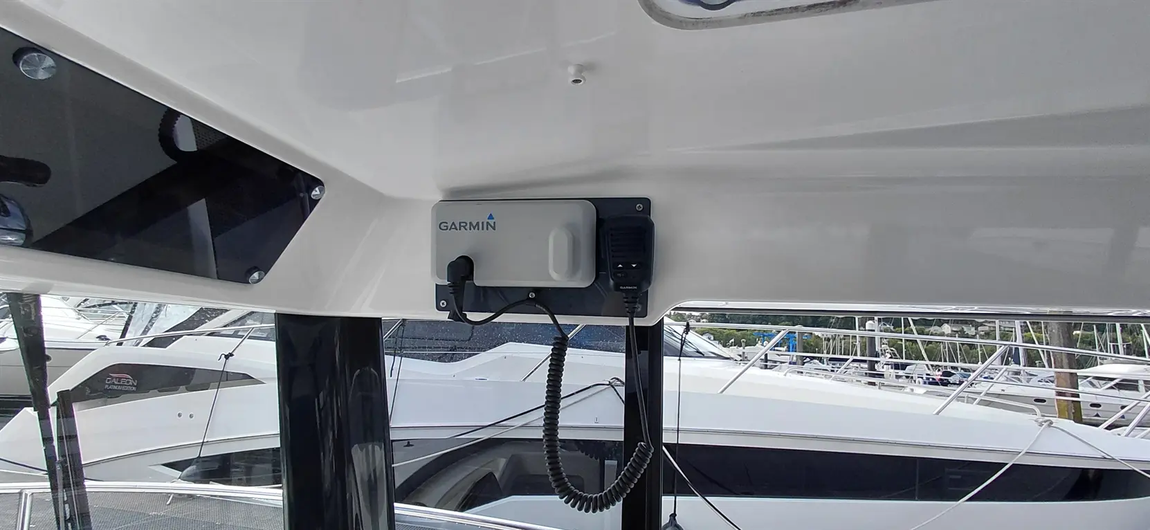 Garmin communication device mounted on a boat with blurred view of other yachts at a marina in the background.