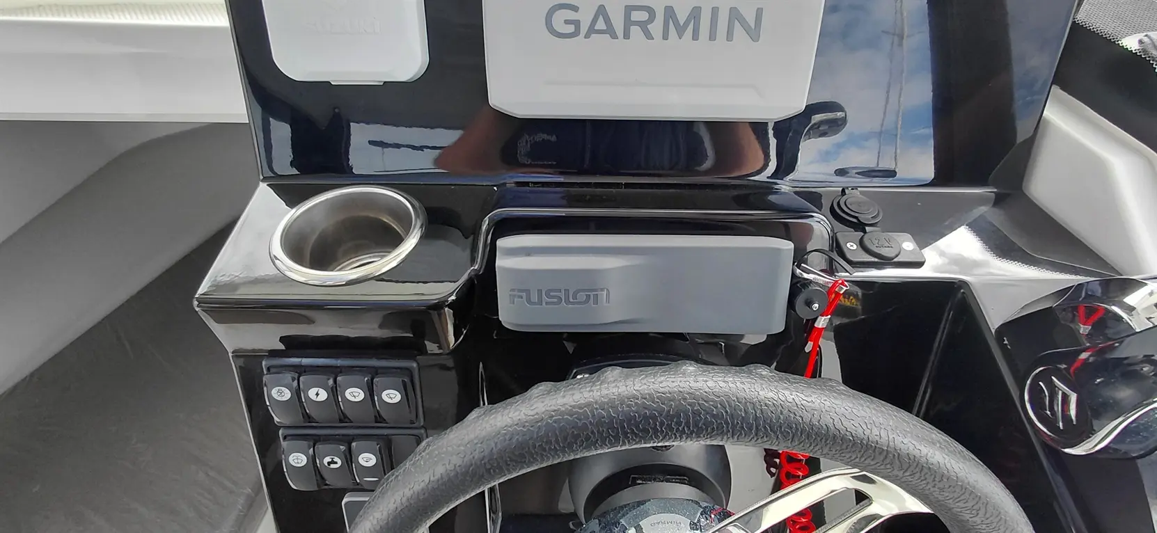 Boat dashboard showing Garmin display, Fusion audio system, controls, and a drink holder, emphasizing sleek marine design.