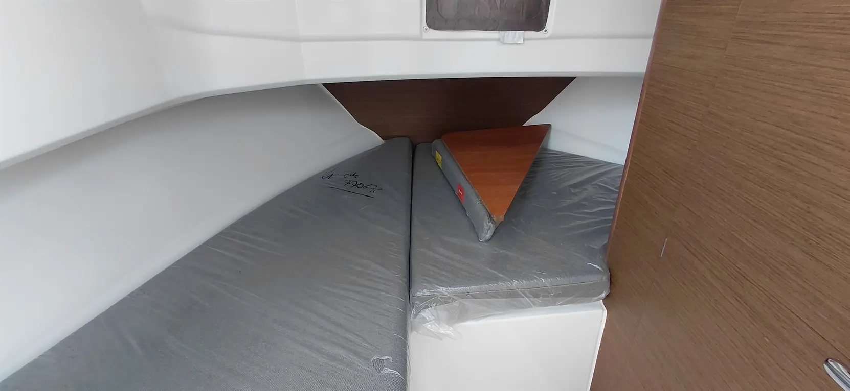 Interior of a boat cabin, featuring two foam mattress pads wrapped in plastic and a wooden triangular table.