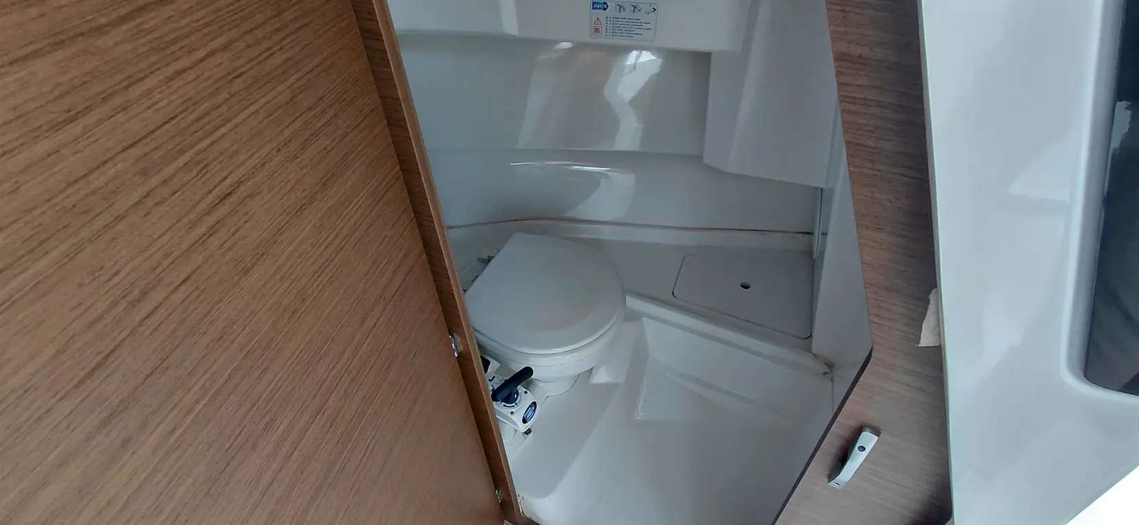 Compact bathroom featuring a white toilet, wooden wall, and control mechanism, emphasizing cleanliness and efficiency.