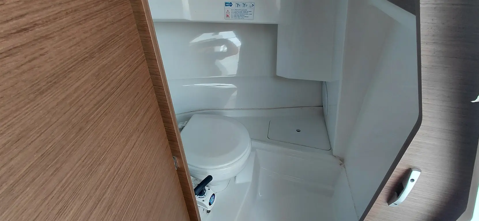 Compact bathroom with a white toilet, wooden door, and instructions on the wall for the toilet's operation.
