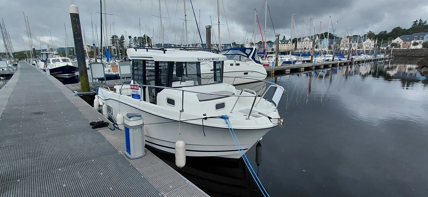 A white boat named "Second Wind" is docked in a marina, with a "For Sale" sign visible, surrounded by other boats.
