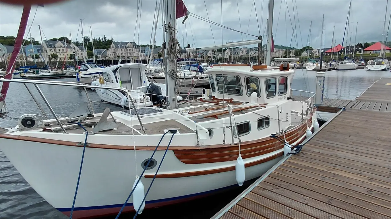 A moored fishing boat with wooden accents in a marina surrounded by various boats and grey, overcast skies.