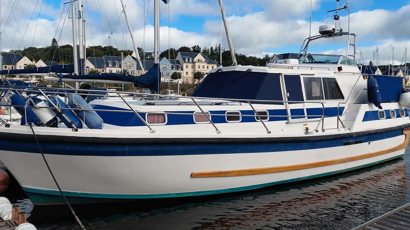 Aquastar 38 motor yacht, marked “AQUA-STAR 1100”, moored in a marina among sailboats.