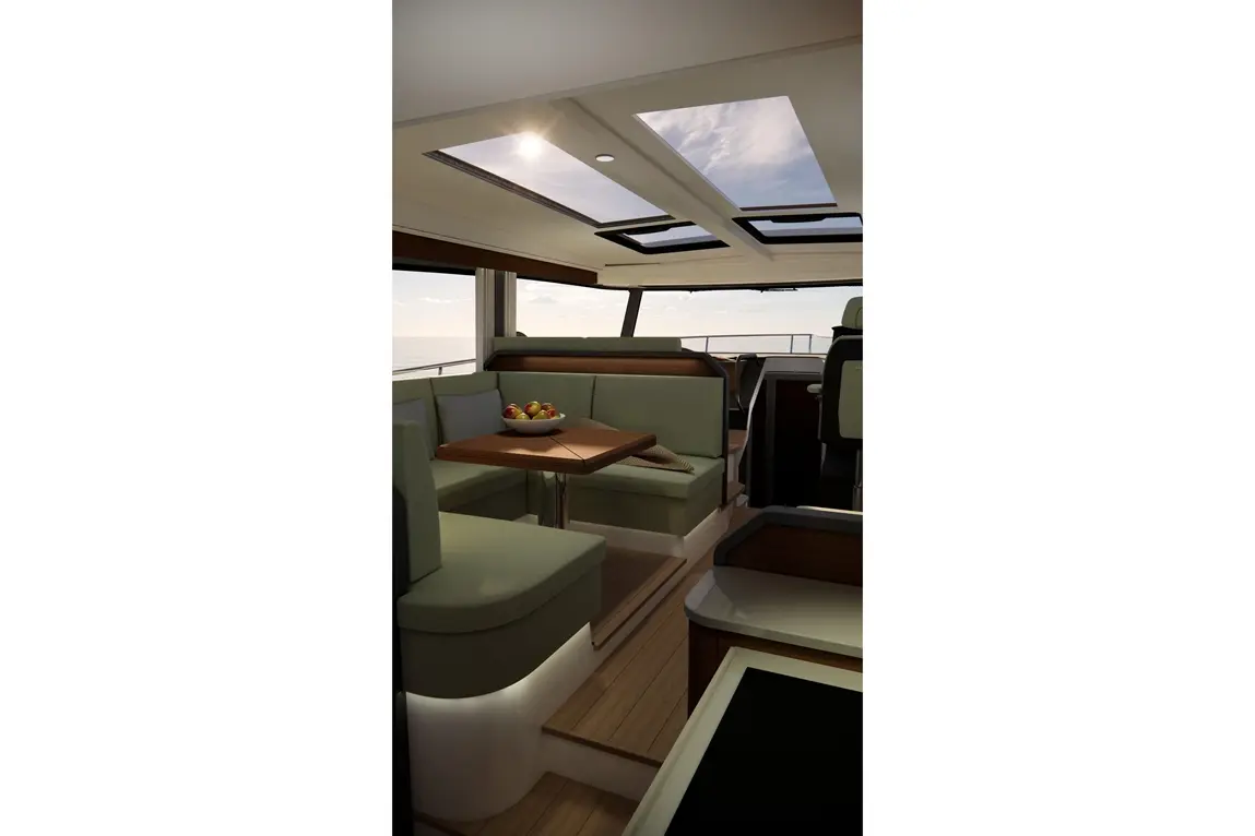 Interior of a yacht featuring a wooden table, green seating, and a bowl of apples, with large windows overlooking the ocean.
