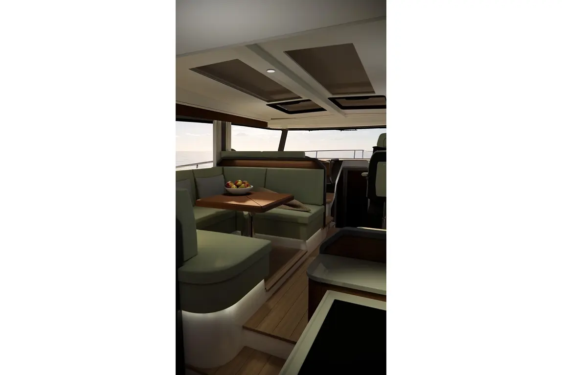 Modern boat interior featuring green seating, a wooden table with a fruit bowl, and views of the sea through large windows.