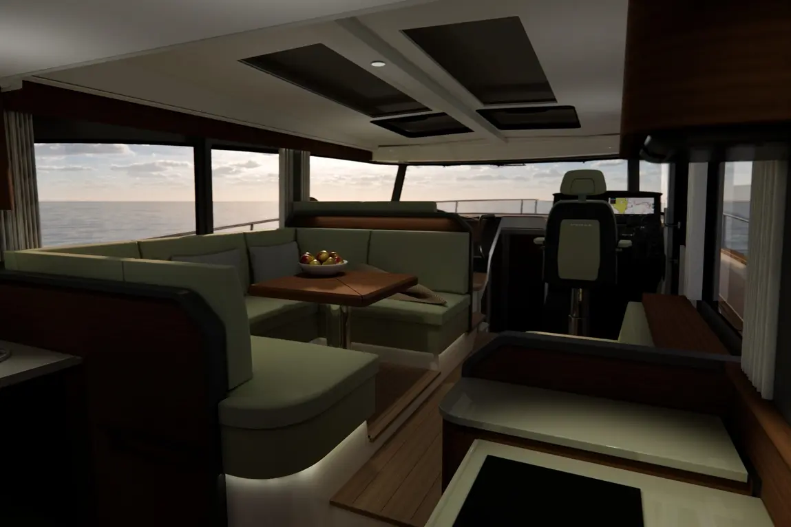 Modern yacht interior with a lounge area, a fruit bowl on a table, and a navigation station. Large windows view the sea.