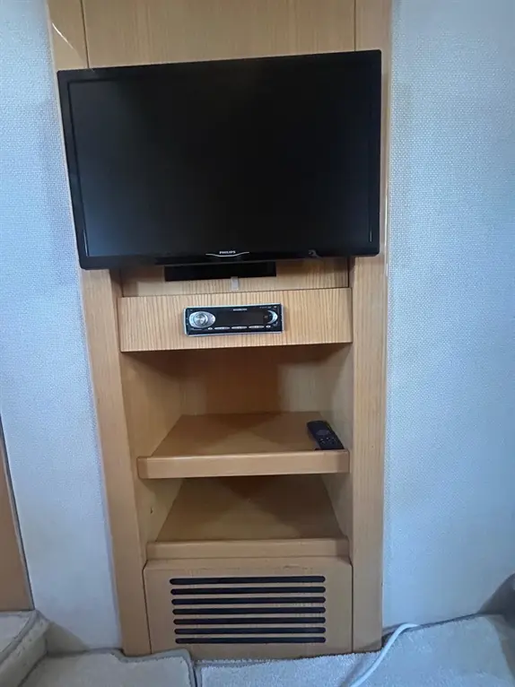 Wooden entertainment unit featuring a Philips TV, audio system, and remote control on shelves, with an air vent below.