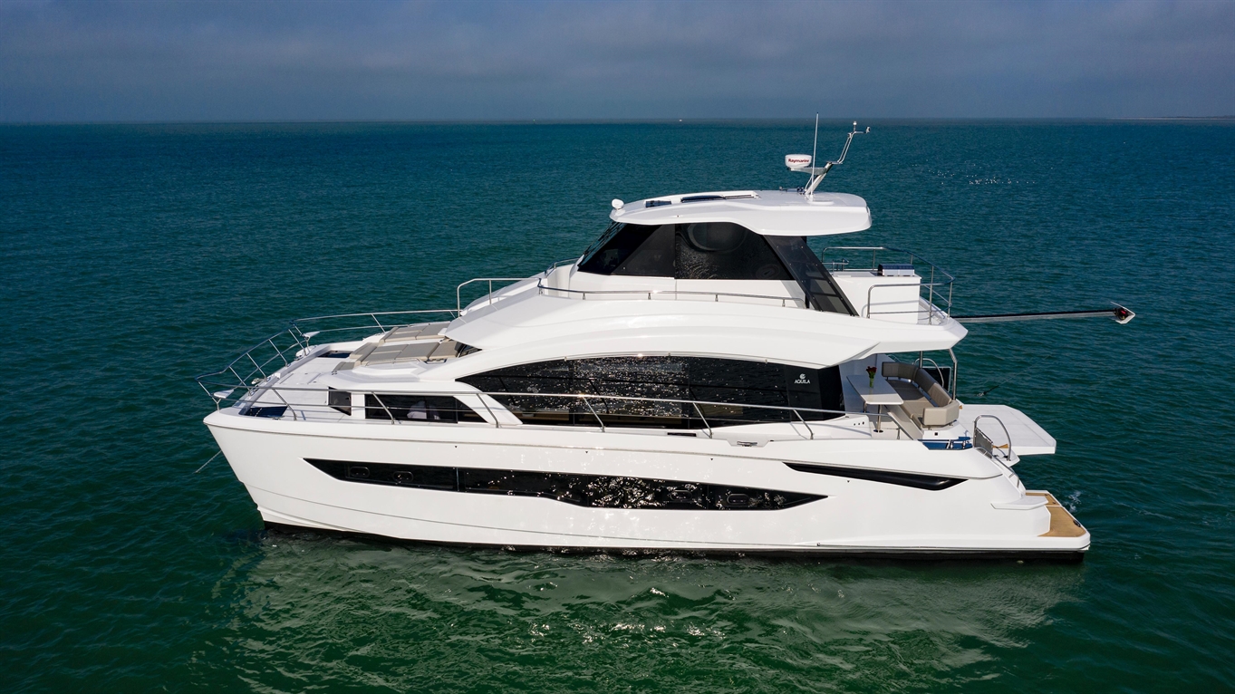 Luxury yacht cruising on clear blue water, featuring a spacious upper deck with lounge area and modern design.