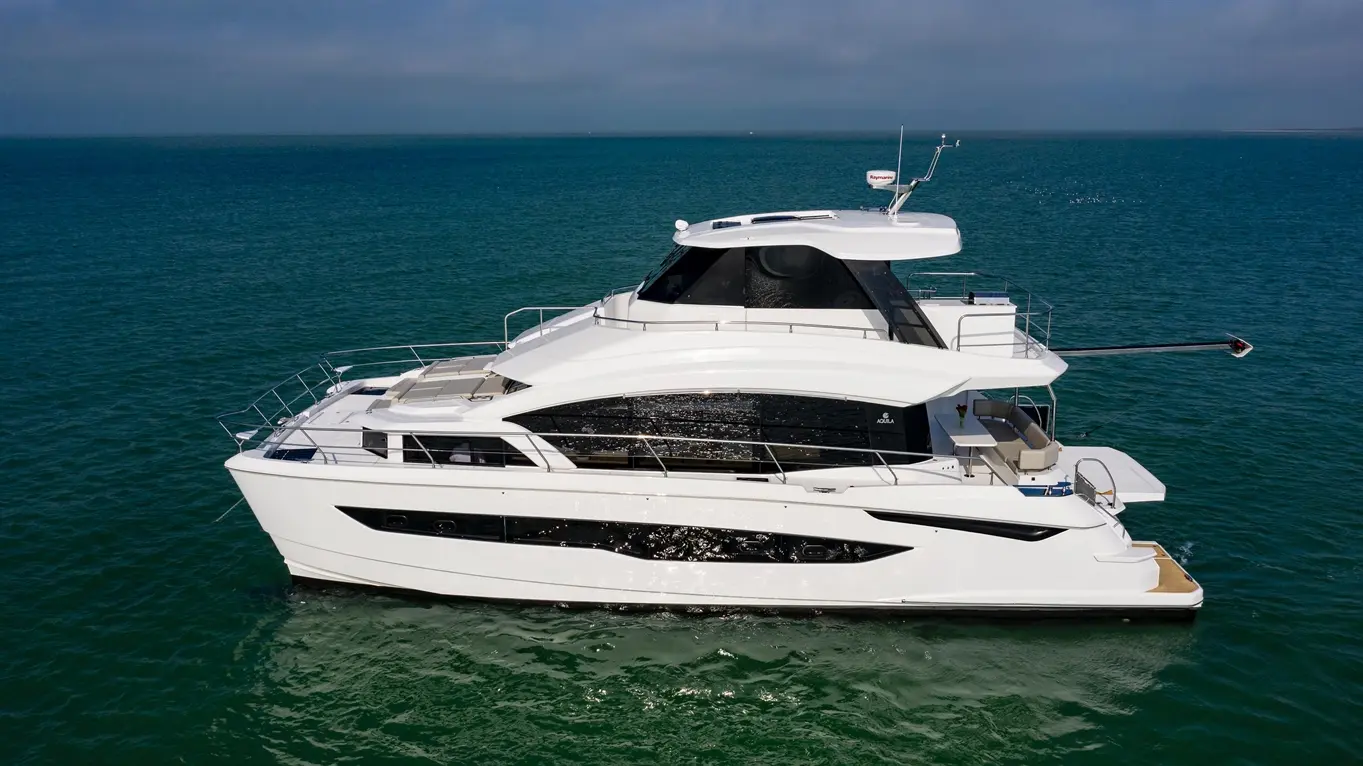 Luxury yacht cruising on clear blue water, featuring a spacious upper deck with lounge area and modern design.