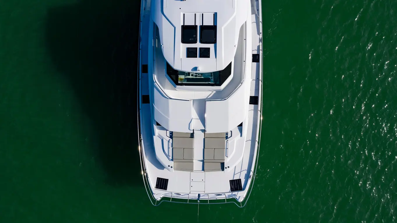 Aerial view of a sleek white yacht with sunbathing areas, anchored in shimmering green waters.
