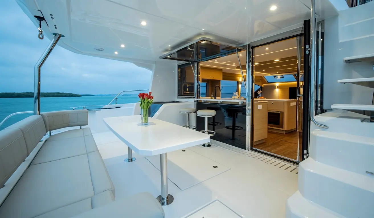 Modern yacht interior featuring a dining area, kitchenette, and ocean view, with a vase of tulips on the table.