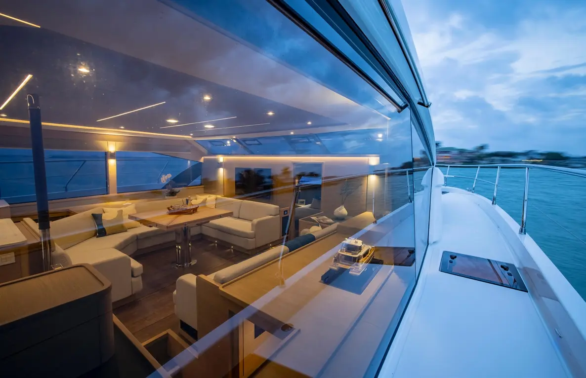 Interior view of a luxury yacht's lounge area with soft furnishings, ambient lighting, and a dining table, reflecting the sea.