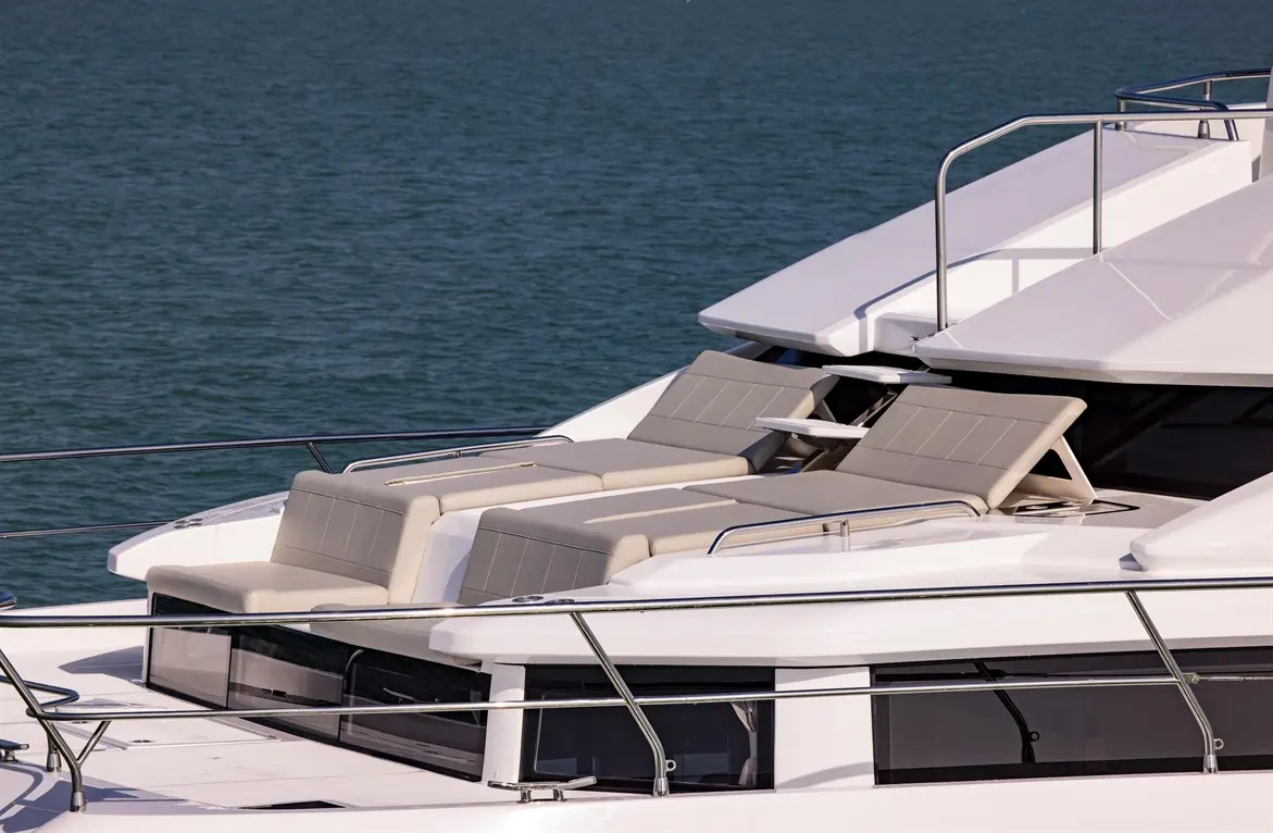 Luxury yacht deck featuring grey lounge chairs, with calm blue waters in the background. Ideal for relaxation and sunbathing.