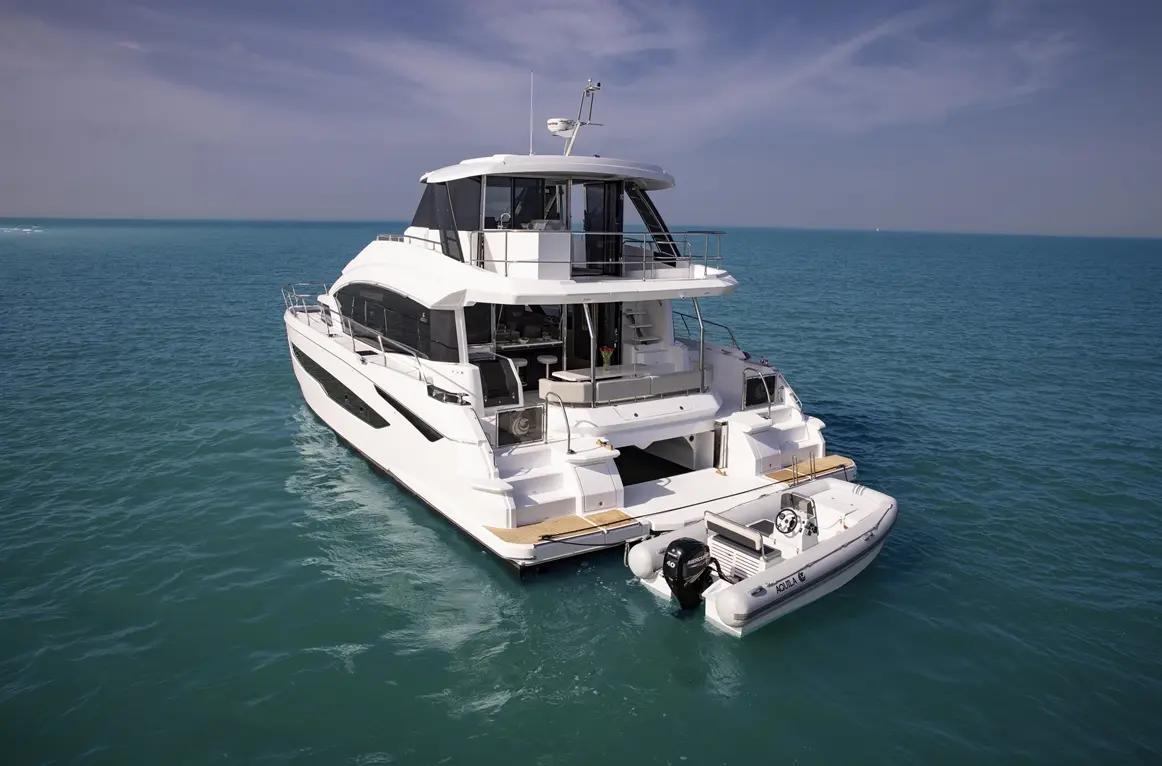 Luxury motor yacht anchored in turquoise waters, featuring a small dinghy and an elegant upper deck for relaxation.