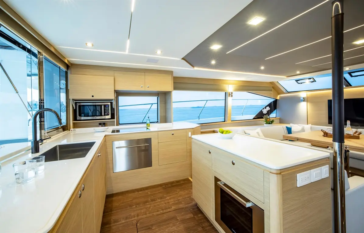 Modern yacht interior kitchen with sleek wooden cabinetry, stainless steel appliances, and a scenic ocean view through large windows.