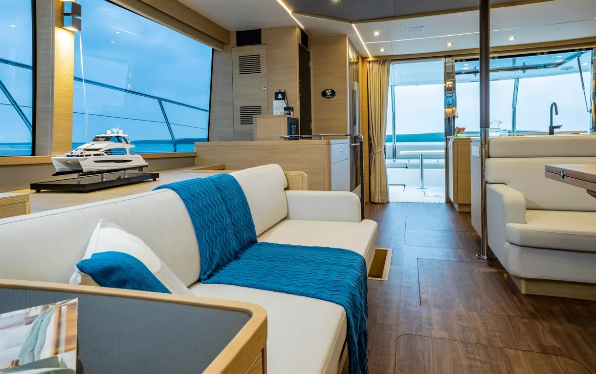 Luxury yacht interior featuring a sleek design, a model yacht, and large windows with ocean views. Soft blue accents.