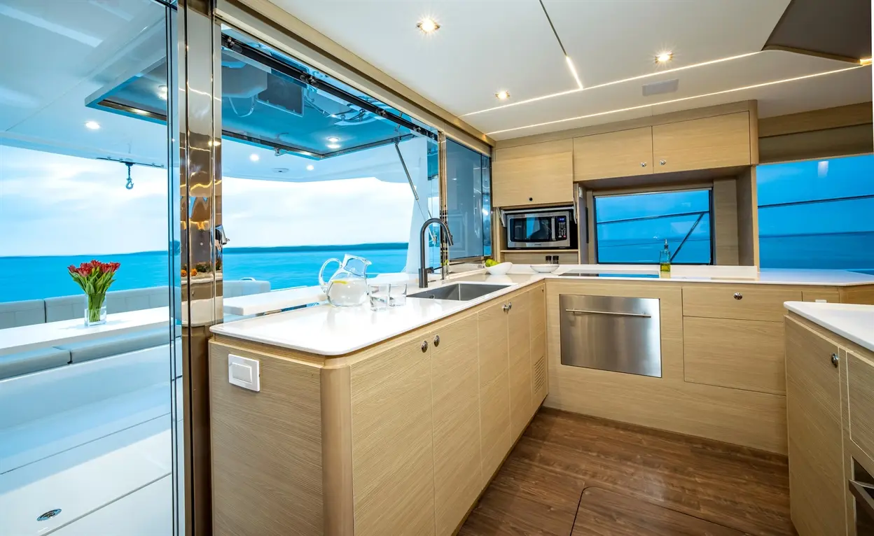 Modern yacht kitchen with sea view, featuring wood cabinetry, stainless steel appliances, and a vase of red tulips.
