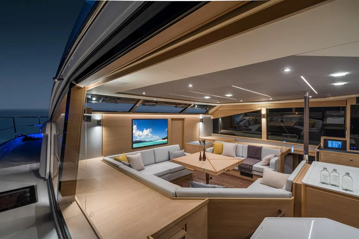Modern yacht interior featuring a spacious lounge with grey sofas, a wooden coffee table, and ocean views through large windows.