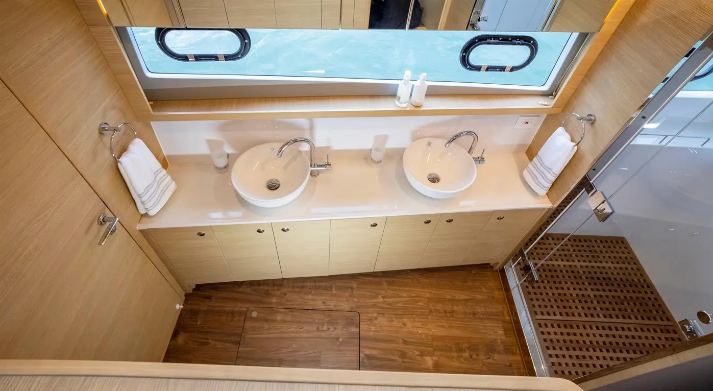 Stylish bathroom with two circular sinks, wooden cabinets, towels, and a view through a circular window.