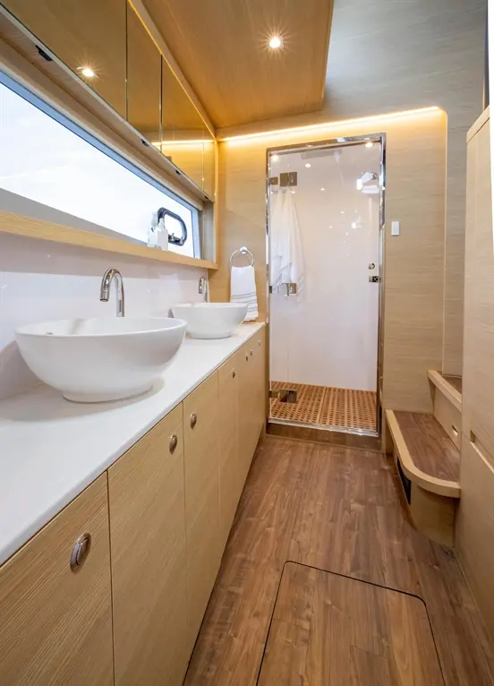 Stylish bathroom with two white basins, wooden cabinetry, a shower cubicle, and a wooden floor, featuring natural light.