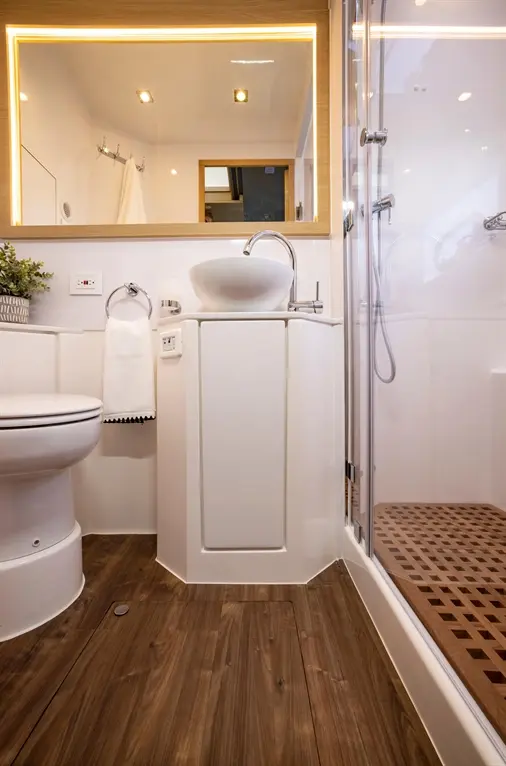 Modern bathroom featuring a white sink, wooden flooring, and a glass shower. Includes a towel holder and illuminated mirror.