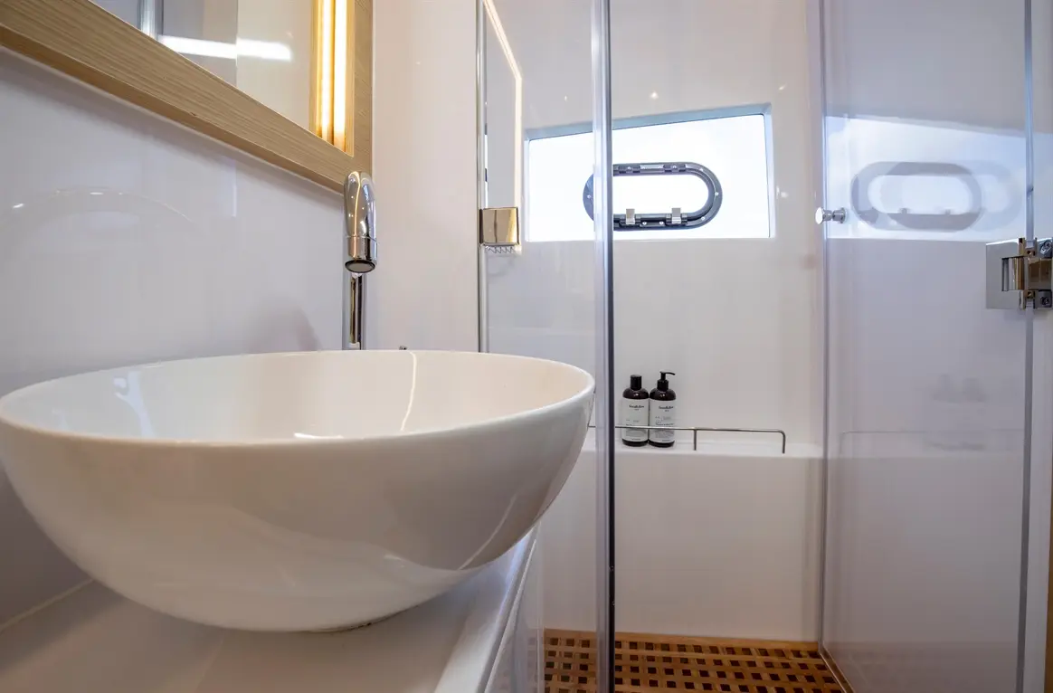 Modern bathroom with a white basin, chrome tap, shower enclosure, and two bottles of toiletries on the tiled ledge.