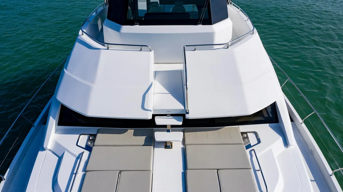 Top view of a luxury boat deck featuring sun loungers, a sleek layout, and clear blue water in the background.