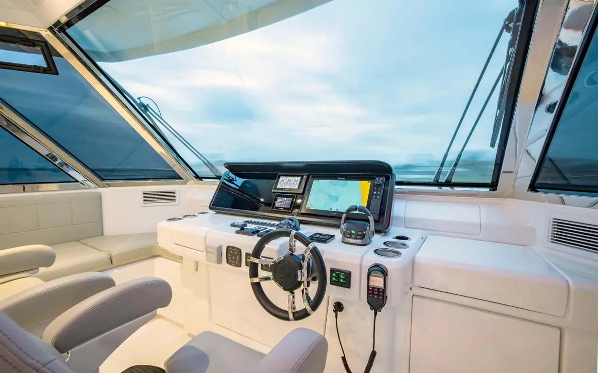 Modern boat dashboard with steering wheel, electronic displays, controls, and panoramic windows showing a cloudy sky.