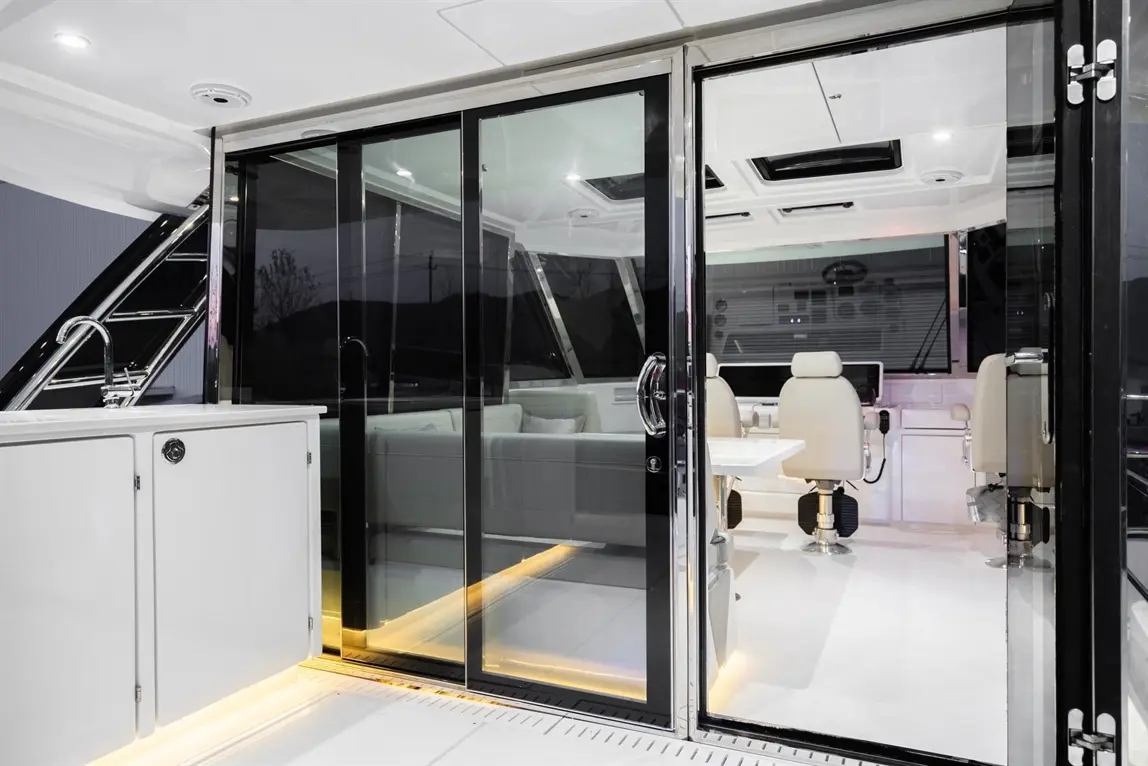 Glass doors open to a stylish interior boat space with a white seating area and sleek furnishings, illuminated softly.
