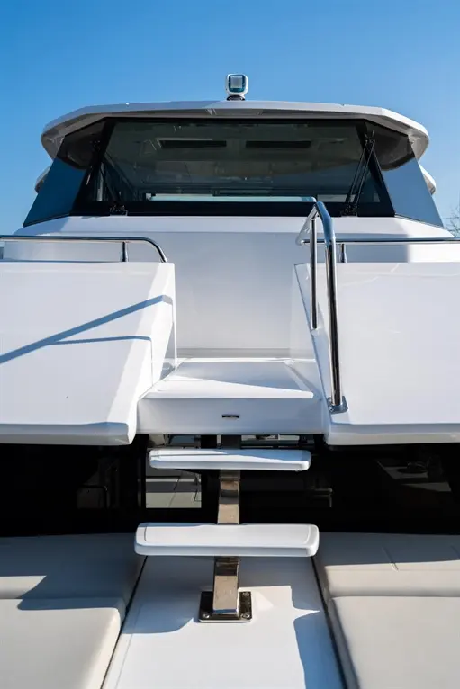 Rear view of a sleek white yacht, featuring steps and a handrail against a clear blue sky.