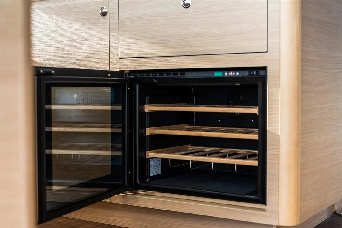 A wine cooler with wooden shelves, open to reveal its interior, positioned within modern cabinetry.