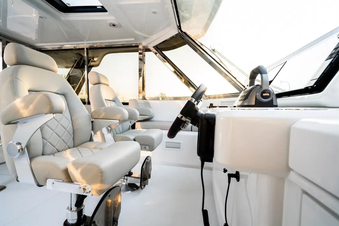 Stylish boat cockpit featuring two grey leather captain's chairs and a steering wheel, with panoramic views through large windows.
