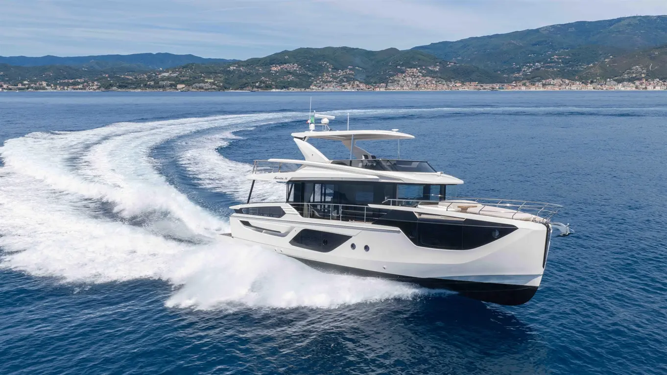 A luxury yacht speeding through clear blue waters, leaving white waves, with a mountainous coastline in the background.
