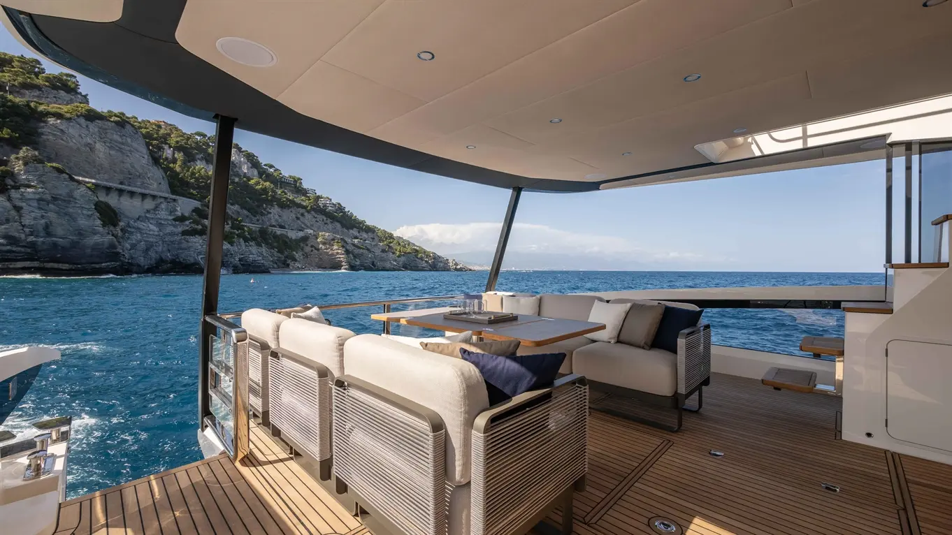 Luxury yacht terrace overlooking the sea, featuring stylish seating, a dining table, and stunning coastal scenery.