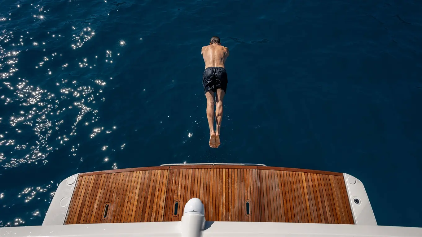 A man dives from a luxury yacht into sparkling blue waters, showcasing an active summer lifestyle at sea.