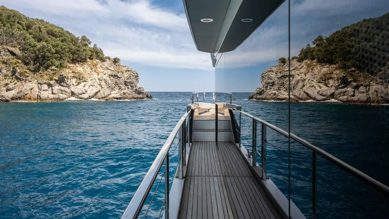 View from a luxury yacht's deck, showcasing rocky cliffs and clear blue water under a sunny sky.