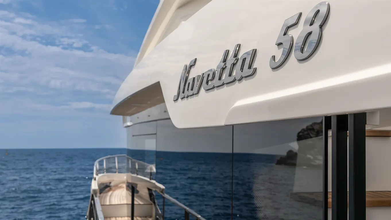Navetta 58 yacht with a sleek design, wooden deck, and ocean view under a clear blue sky.