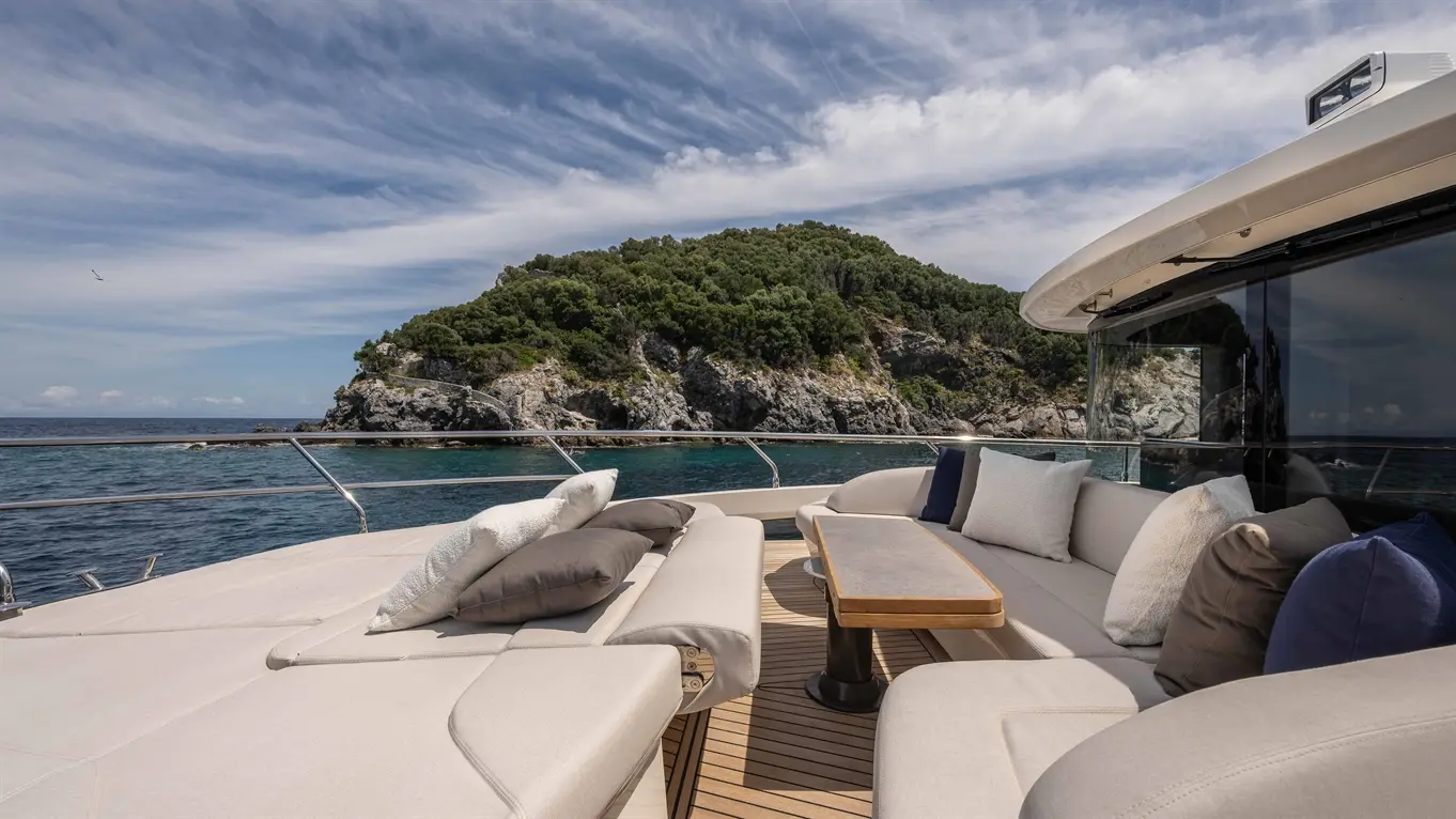 Luxurious yacht deck with plush cushions and wooden table, overlooking tranquil waters and a lush green rocky island.