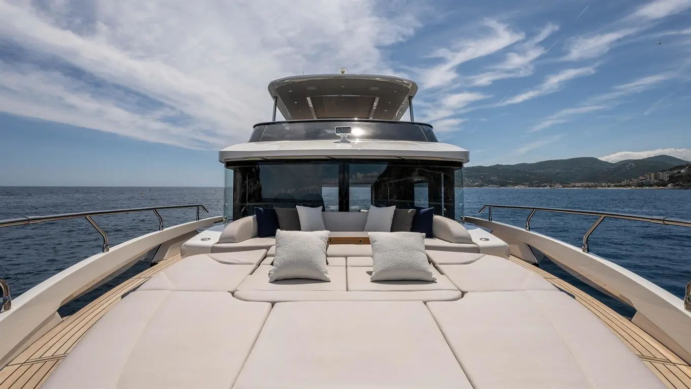 Luxury yacht deck with sun loungers and cushions, overlooking calm sea and distant hills under a blue sky.