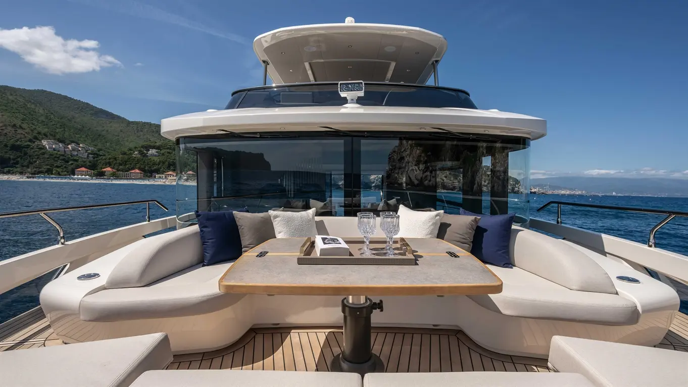 Luxurious yacht deck featuring a round table with glasses, surrounded by plush seating and scenic ocean views.