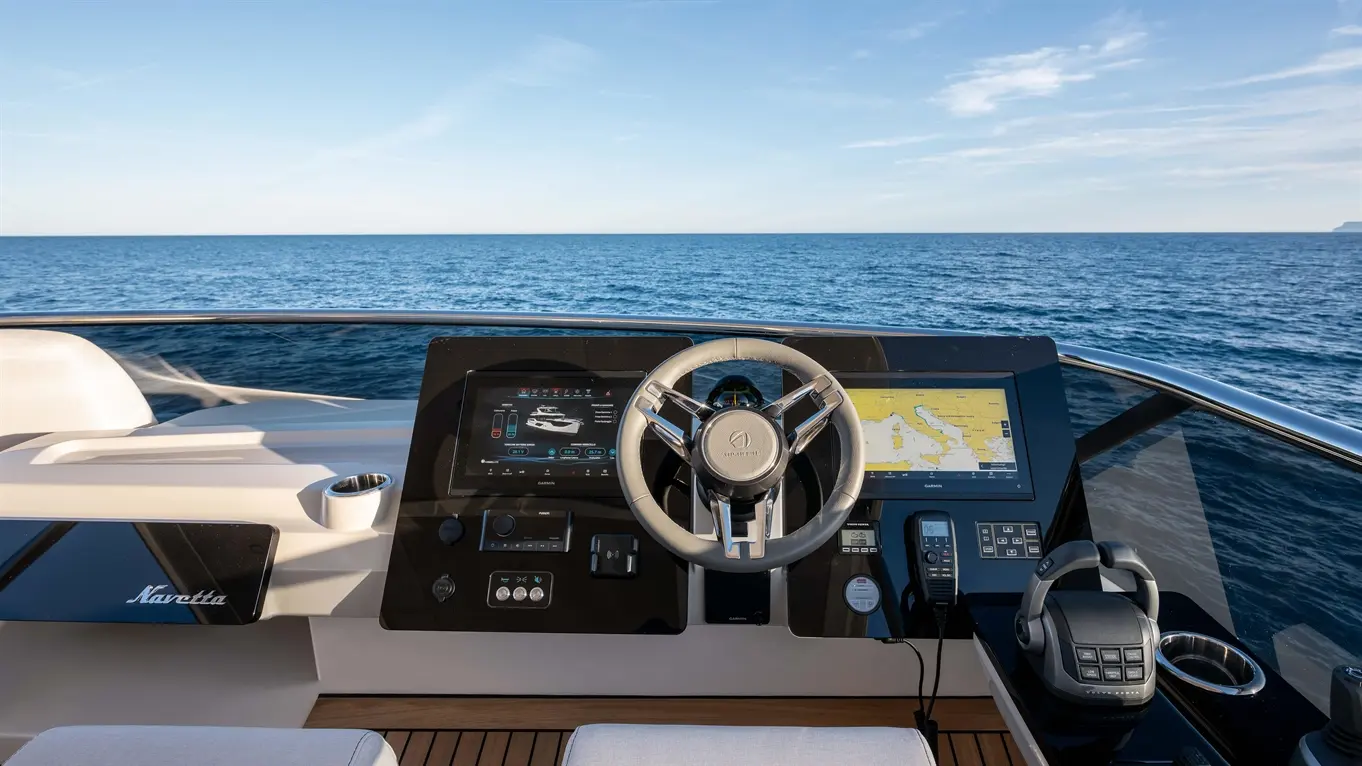 View from a boat's helm, featuring a steering wheel, navigation screen, and equipment against a calm sea backdrop.