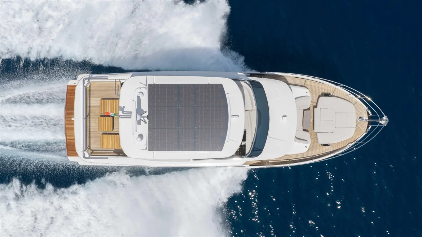 Luxury yacht with solar panels navigating blue waters, leaving a wake, featuring teak deck and comfortable seating.